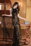 Woman in a black and gold evening gown holding a sheer fabric in an elegant indoor setting.