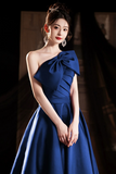 Woman wearing a blue one-shoulder dress with a large bow detail against a dark background