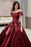 Woman wearing a burgundy off-shoulder gown in an elegant indoor setting.