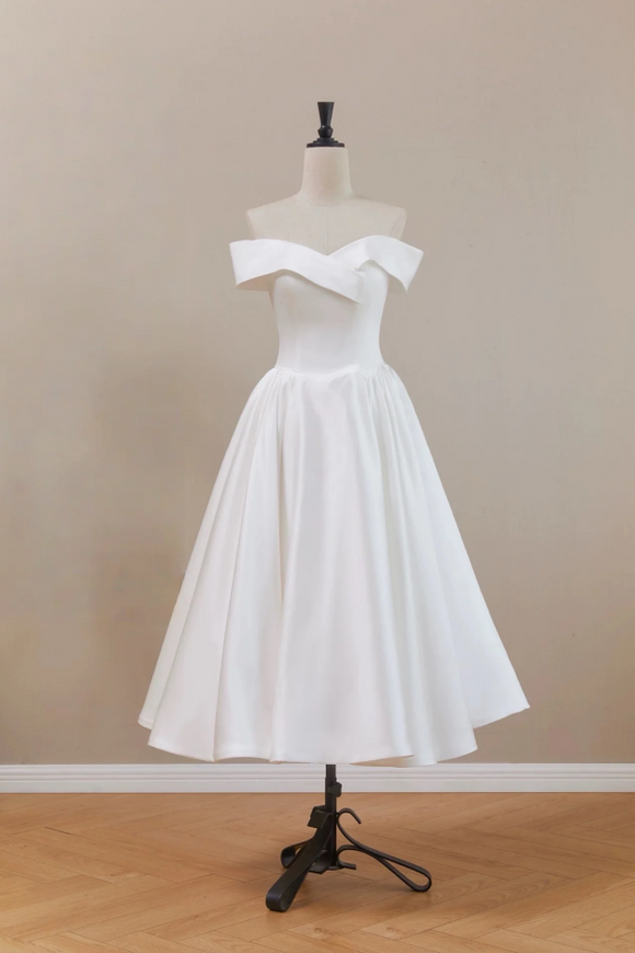White off-shoulder dress on a mannequin against a beige wall.