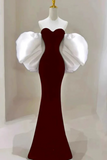 Red evening gown with white puff sleeves on a mannequin against a neutral background