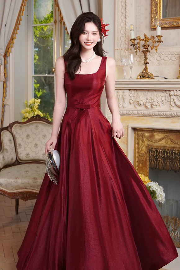 Woman in a burgundy evening gown standing in an elegant room with decorative elements.