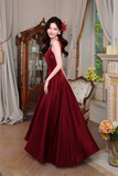 Woman in a burgundy evening gown standing in an elegant room with decorative elements.