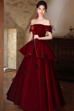 Woman in a red off-shoulder gown holding a red rose in an elegant indoor setting.