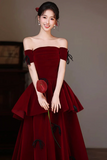Woman wearing a burgundy off-shoulder dress holding a red rose against a neutral background