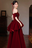 Woman in a burgundy evening gown with a ruffled skirt in an indoor setting.