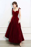 Woman wearing a burgundy evening gown against a white wall.
