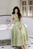 Woman in a green dress standing in a bathroom with a bathtub and tiled floor.