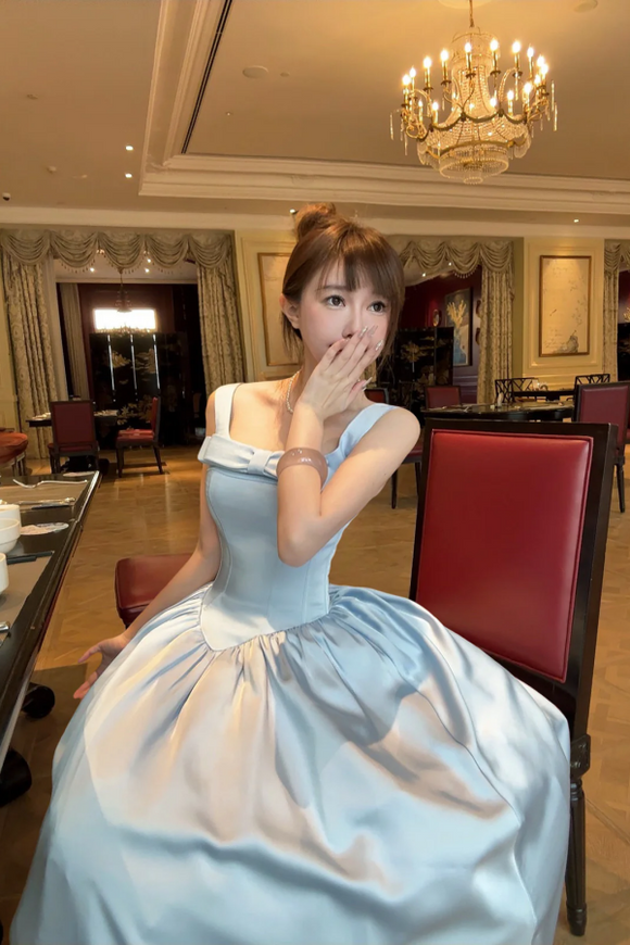 Woman in a light blue dress sitting in a restaurant with a chandelier above.