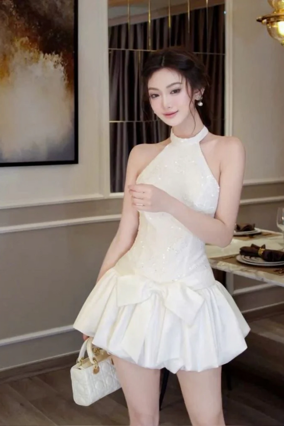 Woman in a white dress standing in an elegant room with a painting on the wall.