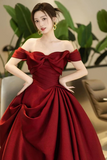 Woman in a red off-shoulder gown posing indoors with plants in the background