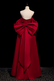 Red evening gown with a large bow on a mannequin against a black background