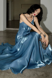 Woman in a blue satin dress sitting on the floor in an indoor setting.