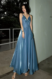 Woman in a blue evening gown standing outdoors against a white wall.