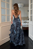 Woman in a blue evening gown standing in a room with a bed and lamp.