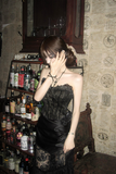 Woman in a black dress standing in a bar with various bottles and decor.
