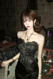 Woman wearing a black lace dress with floral details in a dimly lit room.