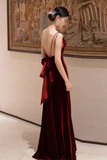 Woman in a burgundy evening gown with a large bow at the back, standing in an art gallery.