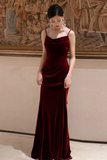 Woman wearing a burgundy velvet evening gown in an indoor setting with a decorative wall in the background.