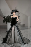 Woman in a black and gray gown with a large hat in an indoor setting