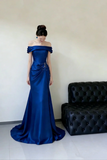 Woman wearing a blue off-shoulder evening gown in a room with a black sofa.