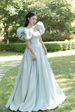 Woman in a light blue dress with puffed sleeves standing in a park.