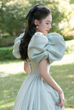 Woman in a light blue dress with puffed sleeves standing outdoors.