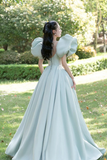 Woman in a light blue gown with puffed sleeves standing in a park.