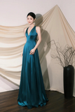 Woman in a teal evening gown standing against a beige curtain.
