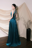 Woman in a teal evening gown standing against a beige curtain.