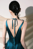 Woman wearing a teal dress with an open back, standing against a neutral background.