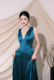 Woman in a teal evening gown standing against a beige curtain.