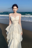 Woman in a white dress standing on a beach with ocean waves in the background