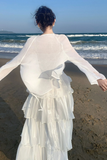 Person in a white dress standing on a beach with ocean waves in the background