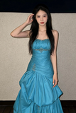 Woman in a blue evening gown posing against a plain background
