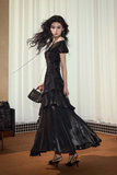 Woman in a black evening gown holding a matching handbag against a neutral background