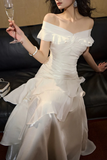 Woman in a white off-shoulder dress holding a glass of champagne.