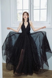 Woman in a black evening gown with sheer overlay standing in a room with large windows.