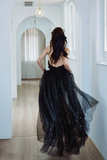 Woman in a black dress standing in a room with light blue walls and wooden floor.