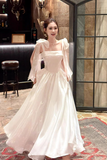 Woman in a white dress standing in an indoor setting with a bar in the background.