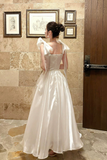 Woman in a white dress standing in a room with framed pictures on the wall.