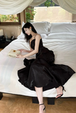 Woman in a black dress sitting on a bed in a bedroom setting