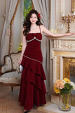 Woman in a burgundy evening gown standing in an elegant room with floral decorations.
