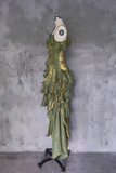 Green ruffled dress on a mannequin against a textured gray wall