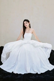 Woman in a white strapless gown sitting on a black couch against a plain background