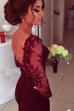 Woman in a burgundy lace dress holding a bouquet of flowers indoors.