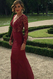 Woman in a burgundy lace dress standing in a garden.