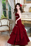 Woman in a red evening gown standing in an elegant room with classical decor.