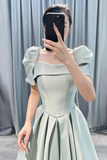 Person wearing a light green off-shoulder dress taking a mirror selfie against a gray curtain background.