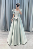 Woman wearing a light blue evening gown with puffed sleeves against a gray curtain background.